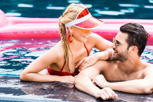 Pareja joven en gafas de sol mirándose unos a otros cerca de la piscina - foto de stock