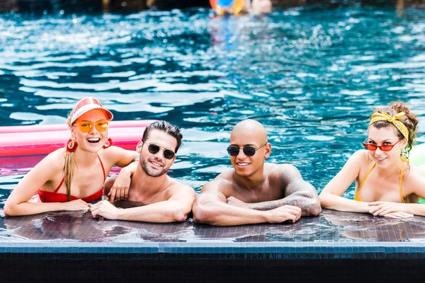 Улыбающиеся друзья в солнечных очках, отдыхающие в бассейне — стоковое фото