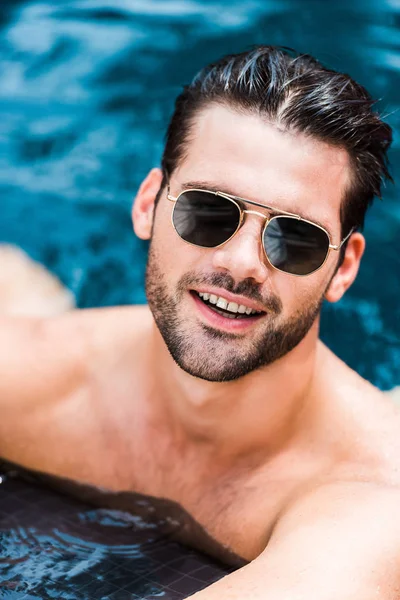 Hombre sonriente guapo en gafas de sol mirando a la cámara cerca de la piscina - foto de stock