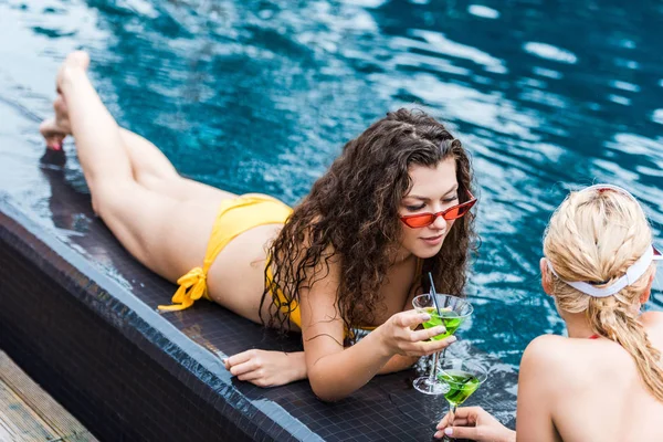 Jovens amigas descansando na beira da piscina com coquetéis verdes — Fotografia de Stock