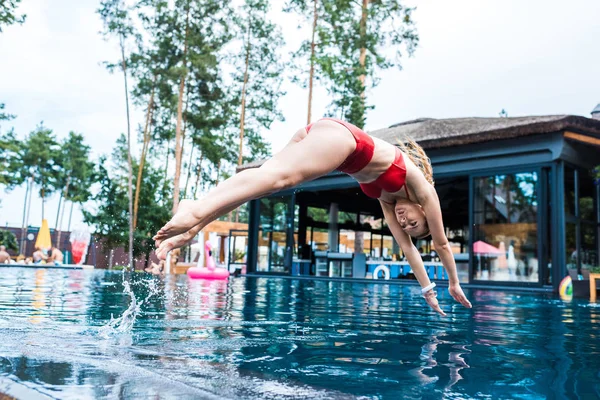 Молода жінка в червоному купальнику стрибає в басейн — стокове фото
