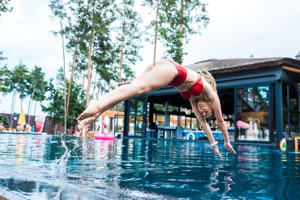 Young woman in red swimsuit jumping into swimming pool — Stock Photo