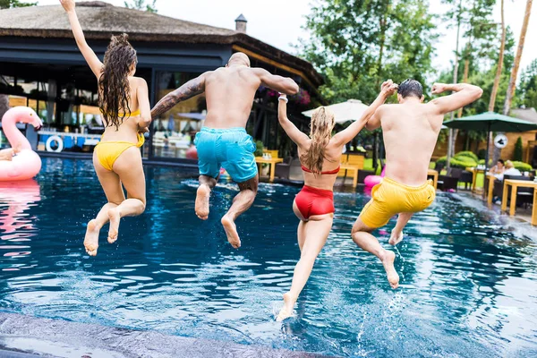 Vista trasera de los jóvenes amigos divirtiéndose y saltando a la piscina - foto de stock