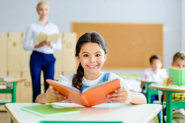 Красивая улыбающаяся школьница смотрит в камеру во время чтения книги — стоковое фото