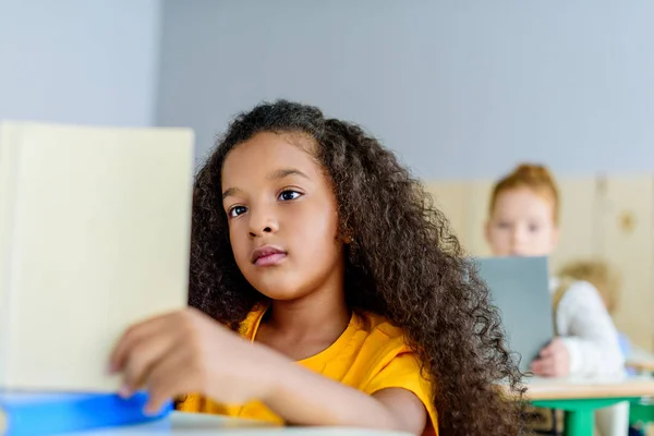 Concentré petite écolière lecture livre pendant la leçon — Photo de stock