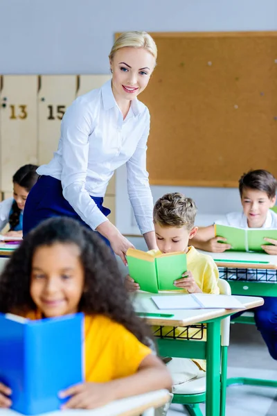 Smiling teacher checking how kids reading books during lesson — Stock Photo