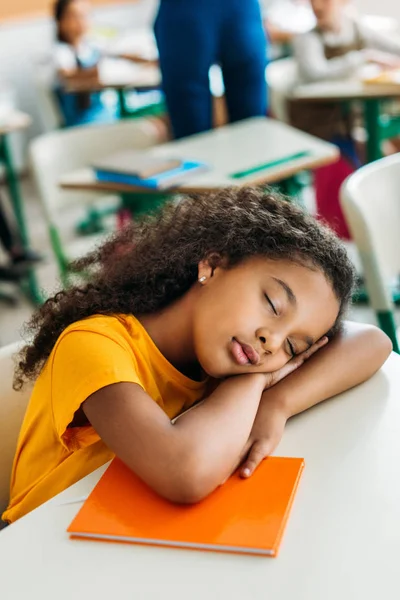 Tired african american schoolgirl sleeping on desk during lesson — Stock Photo