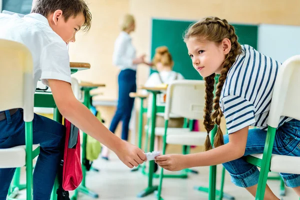 Classmates passing message during lesson while teacher performing lecture — Stock Photo