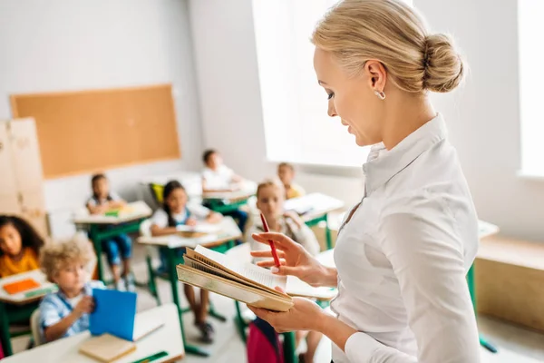 Beautiful teacher reading book for pupils at classroom — Stock Photo