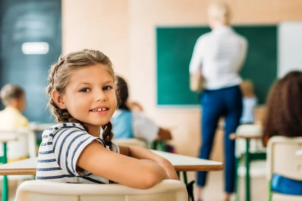 Entzückendes kleines Schulmädchen schaut während des Unterrichts in die Kamera — Stockfoto