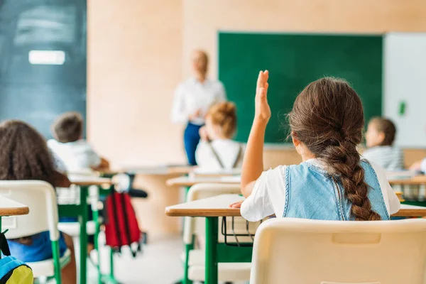 Visão traseira da aluna levantando a mão para responder à pergunta dos professores durante a aula — Fotografia de Stock