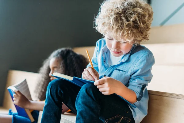 Escolares multiétnicos concentrados que escriben en cuadernos juntos - foto de stock