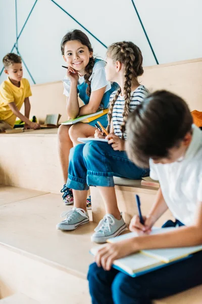 Grupo de escolares com cadernos estudando no tribuno no corredor da escola — Fotografia de Stock