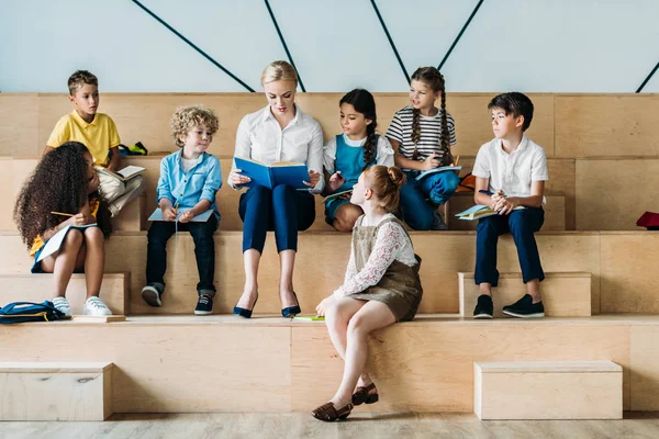 Прелестные счастливые школьники слушают своего учителя, сидя на трибуне — стоковое фото