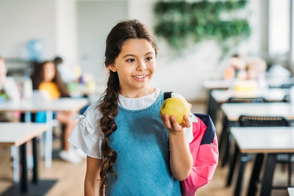 Smiling little schoolgirl with green apple at school cafeteria — Stock Photo