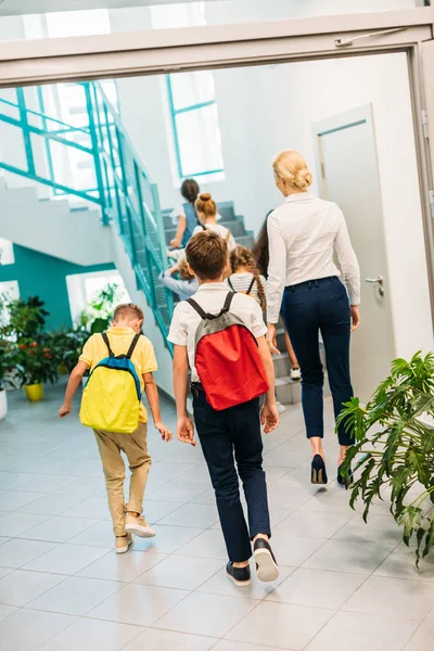 Visão traseira do grupo de estudiosos e professor andando no andar de cima no corredor da escola — Fotografia de Stock