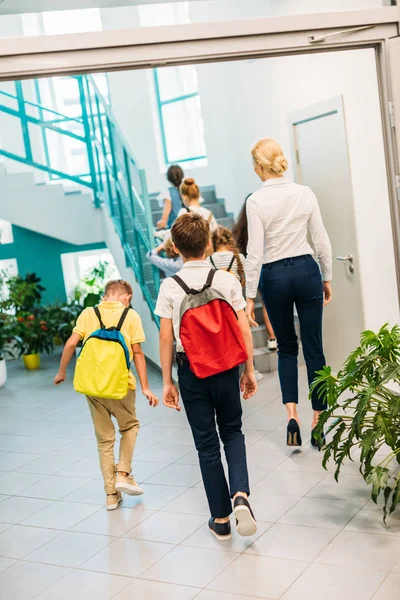 Vista trasera del grupo de eruditos y profesores caminando arriba en el pasillo de la escuela - foto de stock