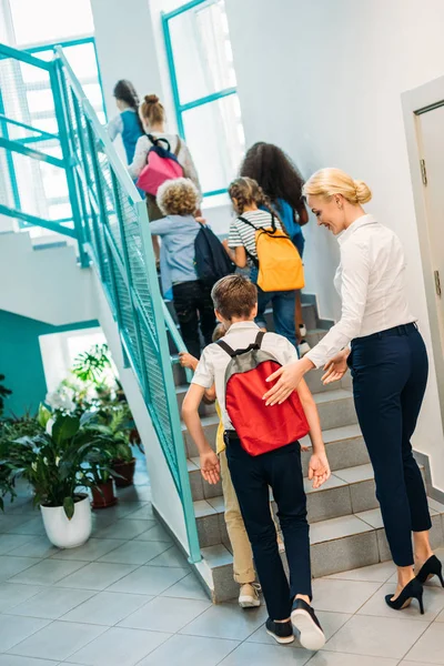 Visão traseira do grupo de alunos e professor caminhando no andar de cima no corredor da escola — Fotografia de Stock