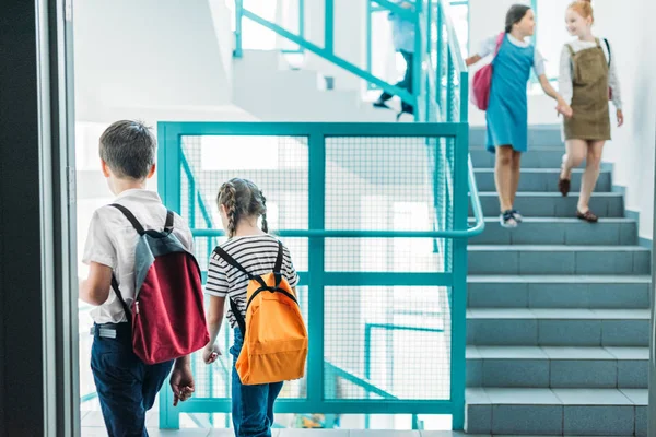 Compañeros de clase de edad elemental caminando escaleras abajo en la escuela - foto de stock