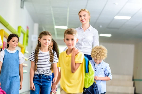 Gruppo di scolari felici e insegnante che cammina lungo il corridoio scolastico — Foto stock