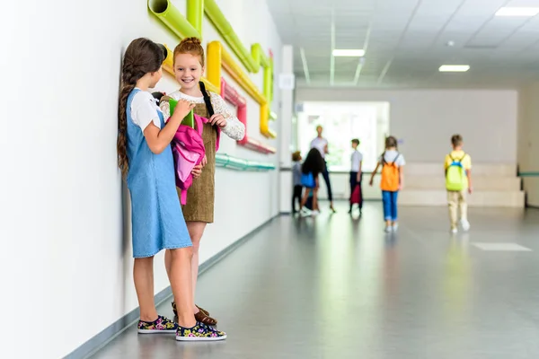 Two happy schoolgirls chatting at school corridor during break — Stock Photo