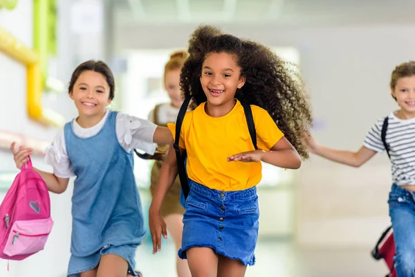 Прелестные счастливые школьники, бегущие по школьному коридору вместе — стоковое фото