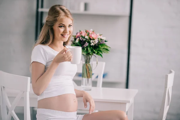 Retrato de mujer embarazada feliz con taza de té en casa - foto de stock