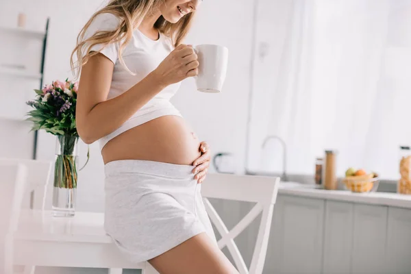 Plan recadré de la femme enceinte avec tasse de thé toucher le ventre à la maison — Photo de stock