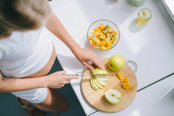 Overhead view of pregnant woman with knife cooking fruits salad at home — Stock Photo