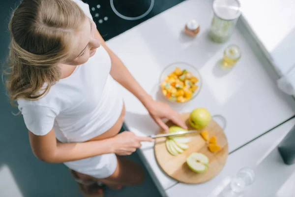 Vista aérea de la mujer embarazada con cuchillo cocina frutas ensalada en casa - foto de stock