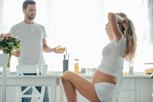 Чоловік приніс фруктовий салат вагітній дружині за столом на кухні — стокове фото