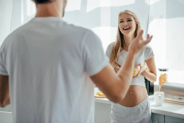 Esposa grávida alegre com salada de frutas e marido na cozinha em casa — Fotografia de Stock