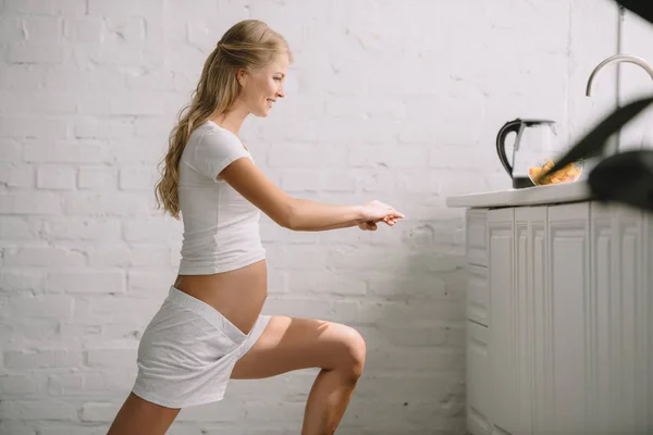 Vue latérale de la femme enceinte souriante faisant des exercices de fitness à la maison — Photo de stock