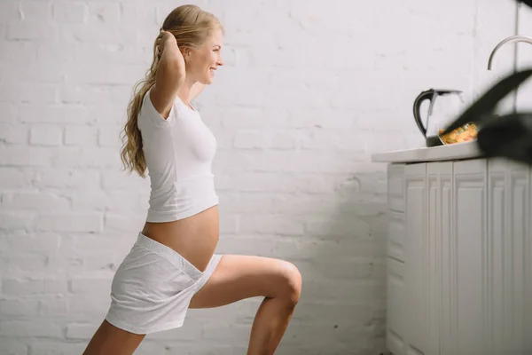 Visão lateral da mulher grávida sorrindo fazendo exercícios de fitness em casa — Fotografia de Stock