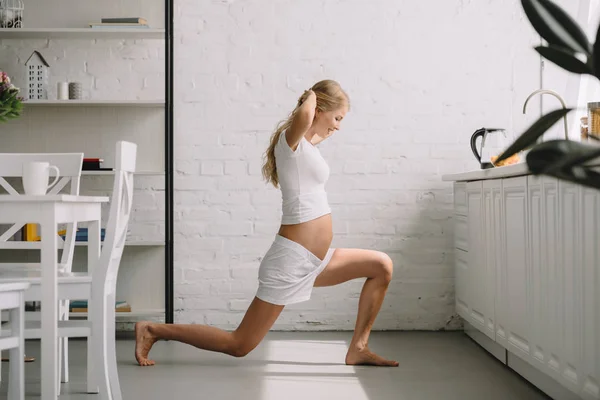 Vista lateral de la mujer embarazada haciendo ejercicios de fitness en casa - foto de stock