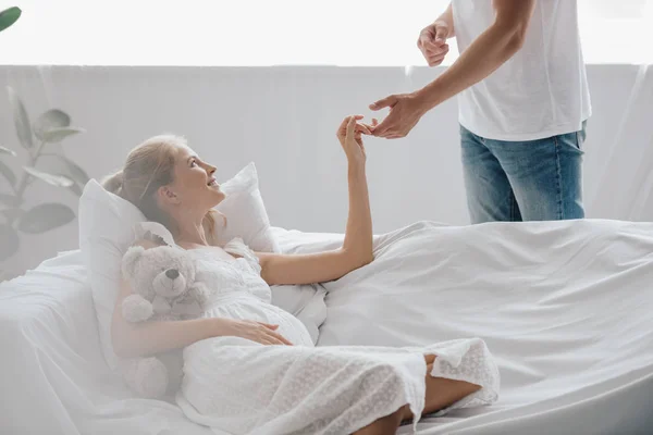 Man and pregnant wife in white nightie on sofa holding hands at home — Stock Photo