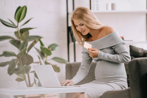 Mujer embarazada con tarjeta de crédito y portátil de compra de bienes en línea en casa - foto de stock