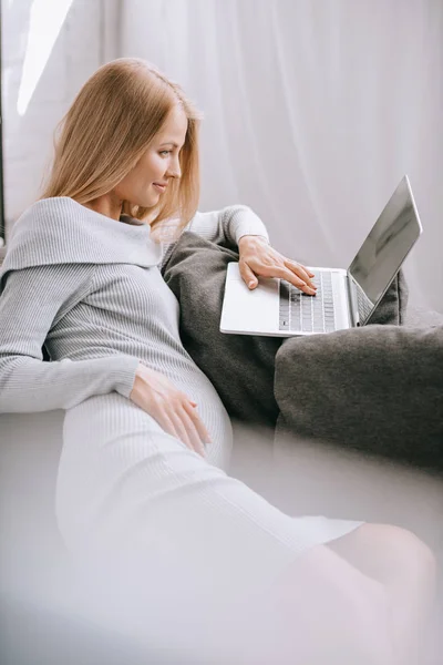 Side view of pregnant woman using laptop on sofa at home — Stock Photo