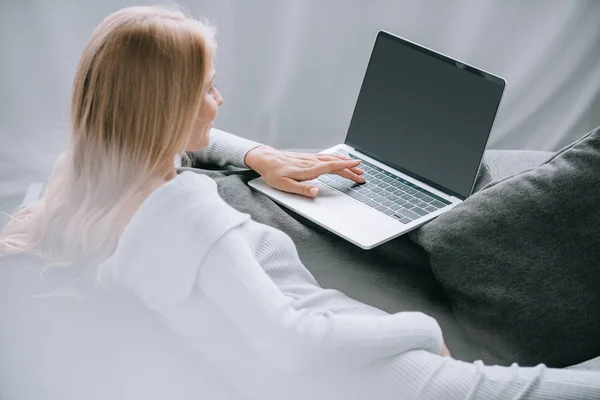 Mujer embarazada usando el ordenador portátil con pantalla en blanco en el sofá en casa - foto de stock