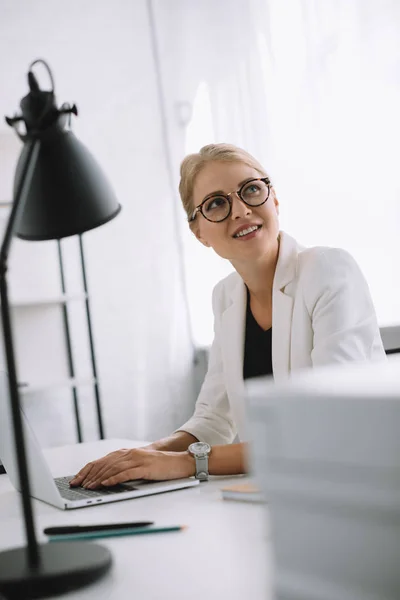 Porträt einer Geschäftsfrau mit Brille, die am Arbeitsplatz mit Laptop im Büro wegschaut — Stockfoto