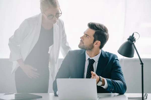 Retrato de la mujer de negocios embarazada y colega en el lugar de trabajo con el ordenador portátil discutir proyecto en la oficina - foto de stock