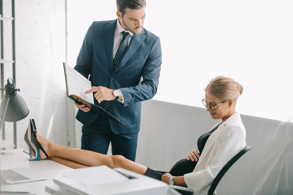 Geschäftsmann mit Dokumenten und schwangere Kollegin diskutieren über Arbeit am Arbeitsplatz im Büro — Stockfoto