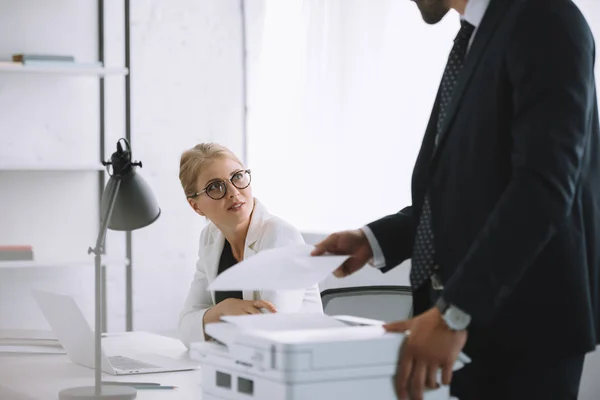 Foyer sélectif de la femme d'affaires dans les lunettes en regardant un collègue avec des papiers à proximité dans le bureau — Photo de stock