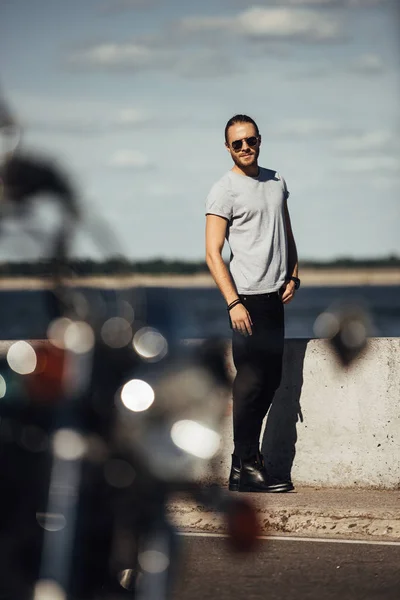 Selective focus of young handsome biker with motorcycle on foreground — Stock Photo