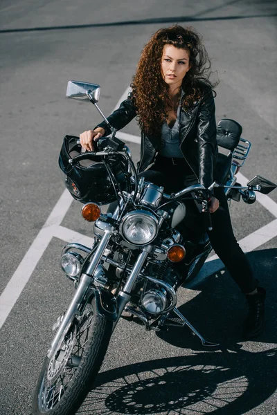 Attraente ragazza riccia seduta sulla moto classica con casco sul parcheggio — Foto stock