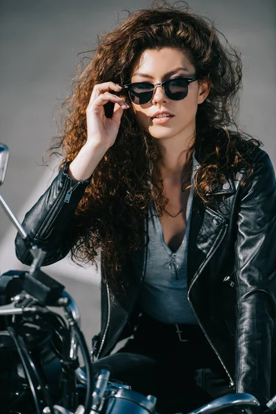 Красивая кудрявая девушка в солнечных очках сидит на мотоцикле — стоковое фото