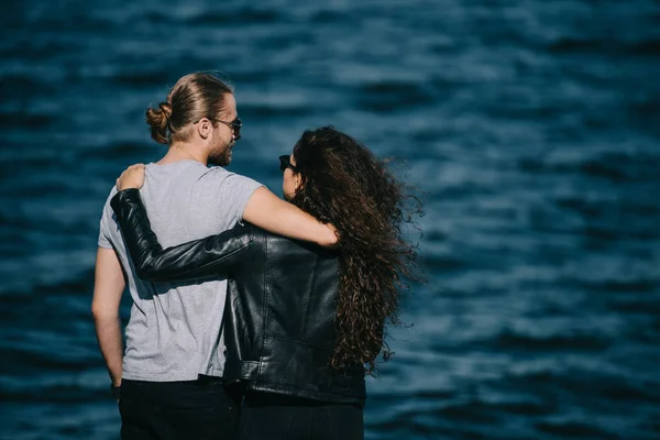Vista trasera de pareja joven abrazándose cerca del mar - foto de stock