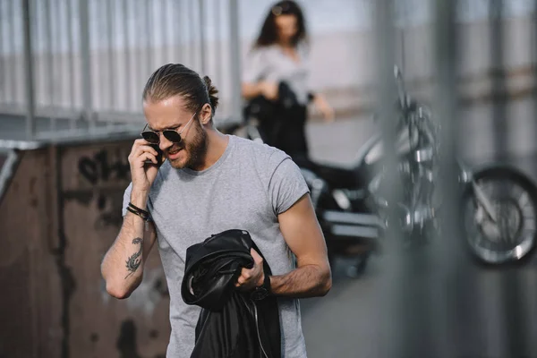 Мужчина разговаривает по смартфону, пока девушка стоит с классическим мотоциклом — стоковое фото