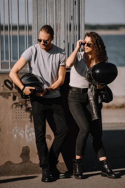 Pareja de jóvenes ciclistas sosteniendo cascos de moto - foto de stock