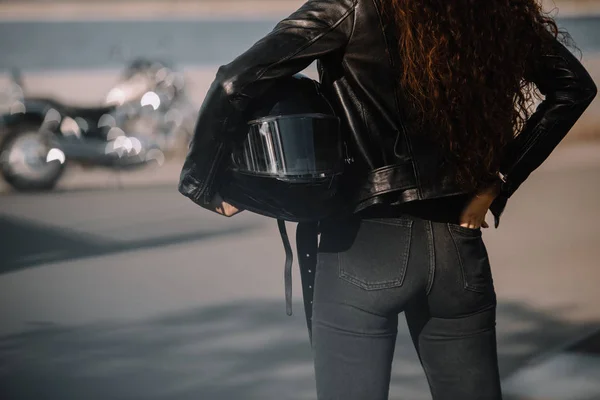 Обрезанный вид женщины, держащей шлем, мотоцикл стоящий на заднем плане — стоковое фото
